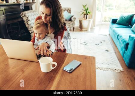Woman sitting with a baby and using laptop. Working mother with her baby at home. Stock Photo