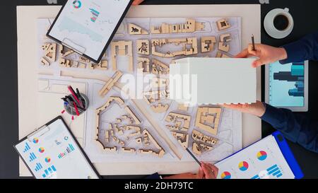 Directly above shot of business people meeting around boardroom table discussing architectural plans for new sustainable shared office space. Engineers brainstorming using modern device on copy space Stock Photo