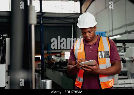 Young african american industrial worker working on digital tablet in the factory - you black male checking modern machinery Stock Photo