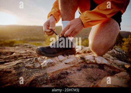 Closeup of hands of fit male jogger tying shoelaces preparing for cross country mountain trail run in nature during sunrise Stock Photo