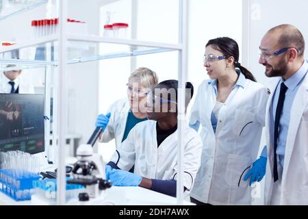 Group of multiethnic pharmacy scientists in lab coats working together in modern facility. Black healthcare researcher in biochemistry laboratory wearing sterile equipment. Stock Photo