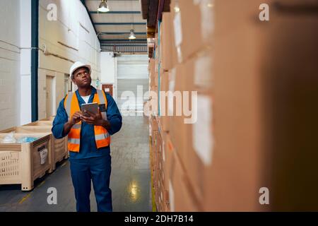 African American factory worker checking stock inventory using digital tablet in modern warehouse Stock Photo