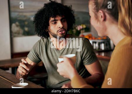Young African American man with an afro in serious conversation with woman while sitting in a cafe and drinking coffee - two diverse friends chatting