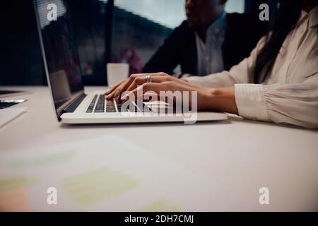 Close-up of businesswoman's hand typing on laptop at workplace during a group meeting in the office Stock Photo
