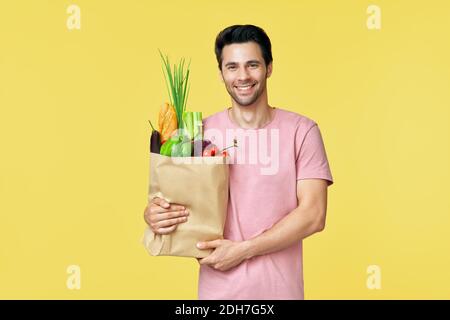 Young handsome man holding paper shopping bag full of fresh vegetables Stock Photo