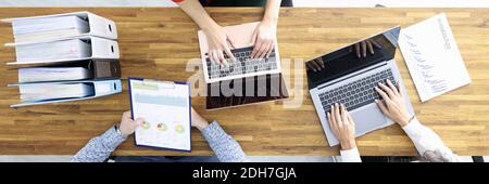 Business man and two women are sitting at wooden table with laptops and documents in office Stock Photo