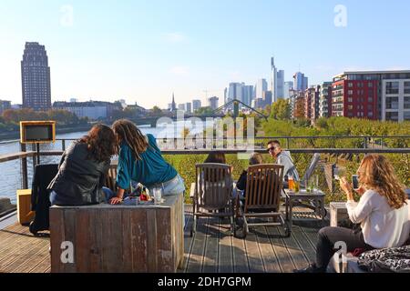 A couple sitting on the rooftop of restaurant Oosten, looking over the park and promenade at River Main, in the background the skyline of Frankfurt. Stock Photo