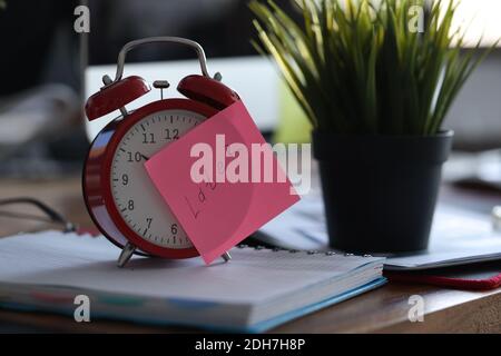 Red alarm clock standing on table near flowerpot in office closeup Stock Photo