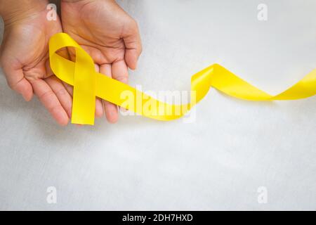 Hand holding Yellow ribbon on white background, copy space. Bone cancer, Sarcoma Awareness, childhood cancer, cholangiocarcinoma, gallbladder cancer, Stock Photo