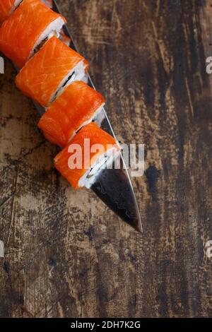 Sushi rolls with vegetables, cheese and salmon are laid out on a knife blade. On a rustic blackboard. Top view