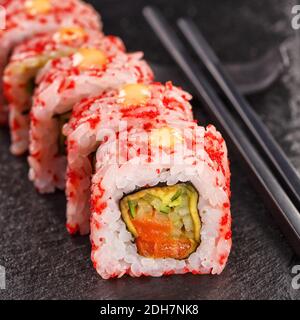 Uramaki sushi rolls covered in red caviar filled with salmon and cucumber. Served on a black stone board. Japanese food. Stock Photo