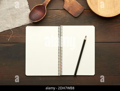 Open notebook with blank white sheets and kitchen utensils on brown wooden table Stock Photo