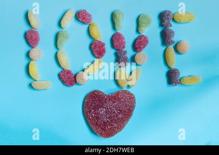 The word love is written with colored candies on a blue background and with a red sugar heart at the bottom. Stock Photo