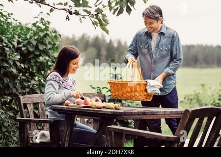 Happy man placing basket on table while woman cutting apples at organic farm Stock Photo