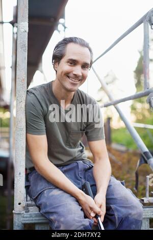 Portrait of smiling man sitting on scaffolding Stock Photo