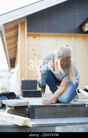 Full length of woman using cordless screwdriver nail into floorboard Stock Photo