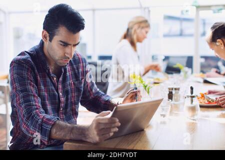 Serious man using digital tablet with friends in background at cafe Stock Photo