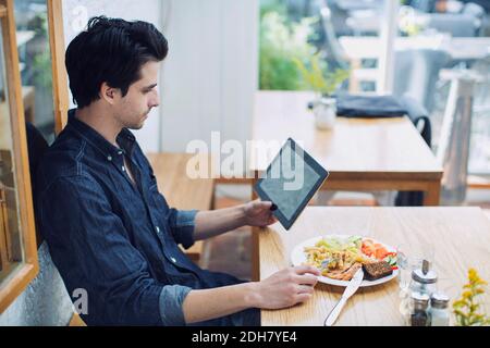 Man using digital tablet while having lunch at cafe Stock Photo