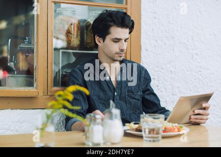Man using digital tablet while having lunch at cafe Stock Photo