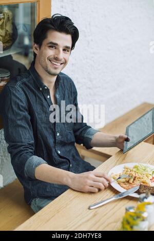 Portrait of happy man using digital tablet while having lunch at cafe Stock Photo