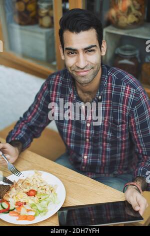 Portrait of smiling man using digital tablet while having lunch at cafe Stock Photo