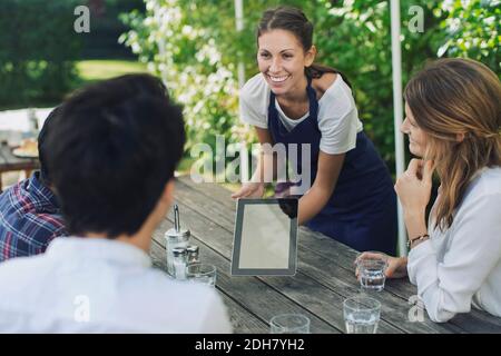 Happy waitress showing menu through digital tablet to people at outdoor restaurant Stock Photo