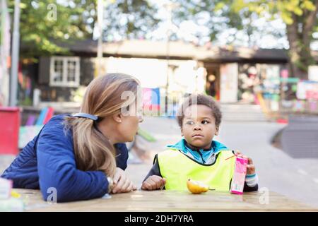 Angry teacher looking at student holding juice box outside kindergarten Stock Photo