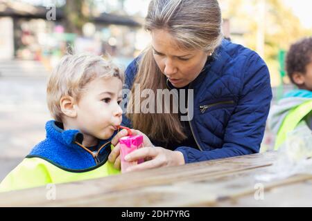 Teacher feeding drink from juice box at table Stock Photo