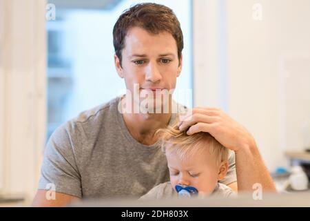 Baby boy sitting with father working on laptop in house Stock Photo