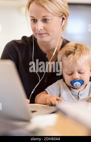 Mother with baby boy listening music on laptop at home Stock Photo