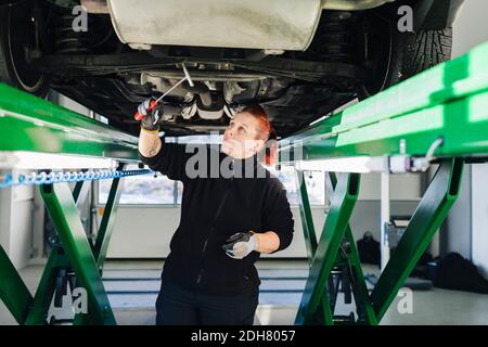 Female mechanic examining car with hammer in auto repair shop Stock Photo