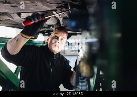 Female mechanic examining car with hammer in auto repair shop Stock Photo