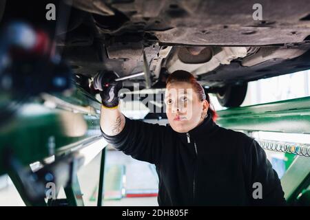 Female mechanic examining car with hammer in auto repair shop Stock Photo