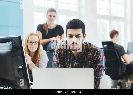 Businesswomen looking at male colleague using laptop at desk in creative office Stock Photo