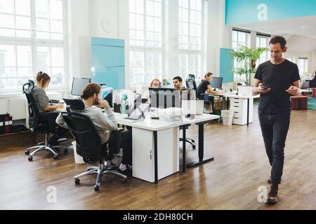 Businessman walking by colleagues working at desk in creative office Stock Photo