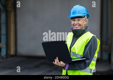 Portrait of happy mature female worker using laptop at factory Stock Photo