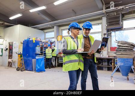 Male and female workers using laptops in factory Stock Photo