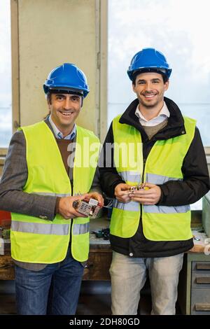 Portrait of confident manual workers holding machine part in factory Stock Photo