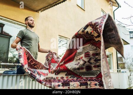 Man dusting carpet while standing on balcony Stock Photo