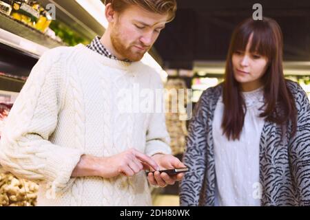 Young couple using smart phone in supermarket Stock Photo