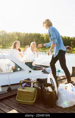Friends unloading luggage from boat on pier against clear sky Stock Photo