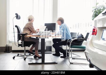 Saleswoman explaining documents at desk to man in car dealership Stock Photo