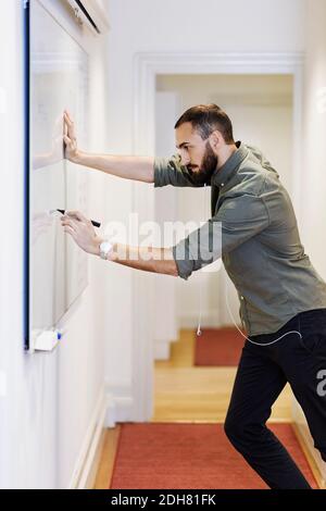 Side view of businessman writing on whiteboard in office Stock Photo