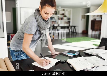 Female architect reading book at table in home office Stock Photo