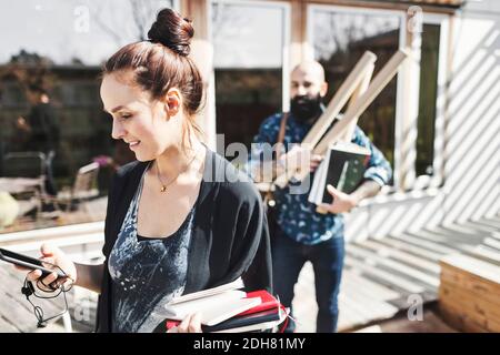 Smiling architect using mobile phone while colleague holding blueprints in background at yard Stock Photo