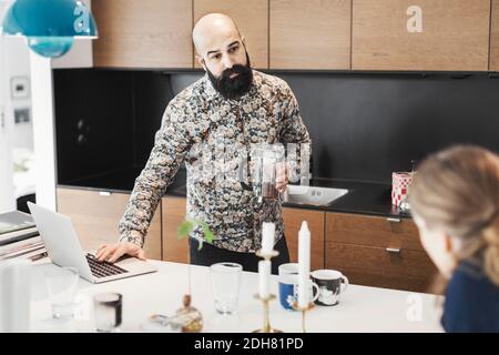 Male architect looking at woman while using laptop in kitchen Stock Photo