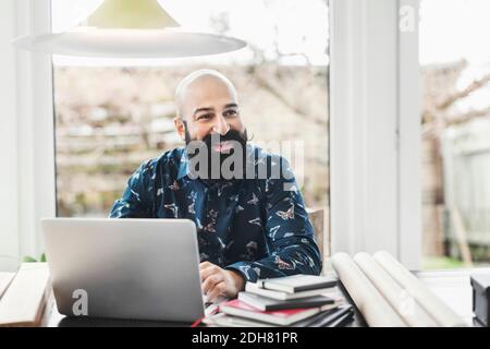 Happy male architect looking away while using laptop at home office Stock Photo