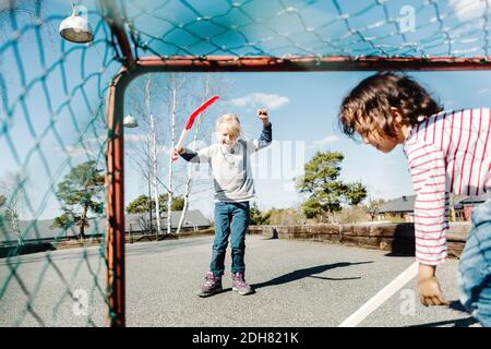 Excited girl gesturing while playing hockey with boy at yard Stock Photo