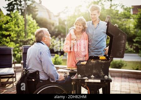 Family looking at disabled man barbecuing at yard Stock Photo