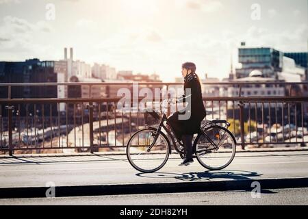 Side view of businesswoman riding bicycle on bridge in city Stock Photo